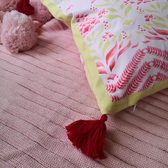 Close-up of pillow edge showing red floral print and red tassel on a pink ribbed blanket.