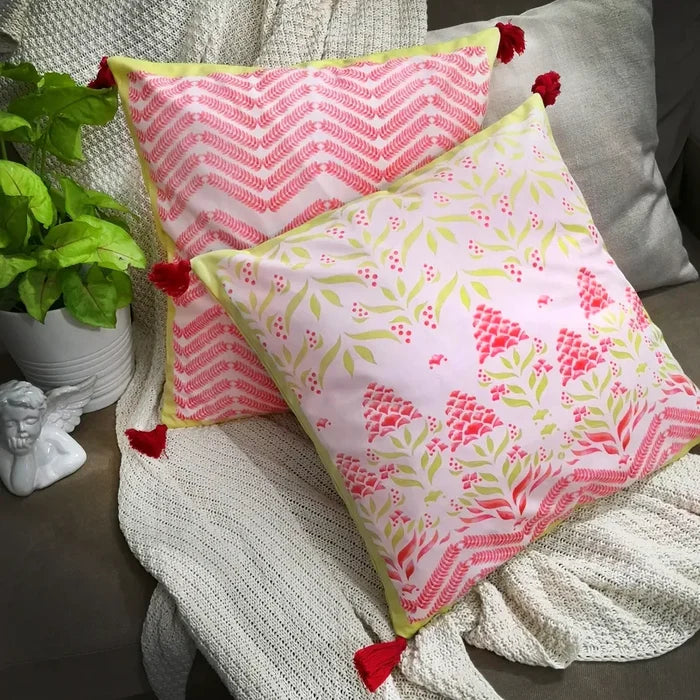 Two decorative pillows, one floral print and one with a red chevron pattern, both with red tassels, on a blanket with a statue and plant.