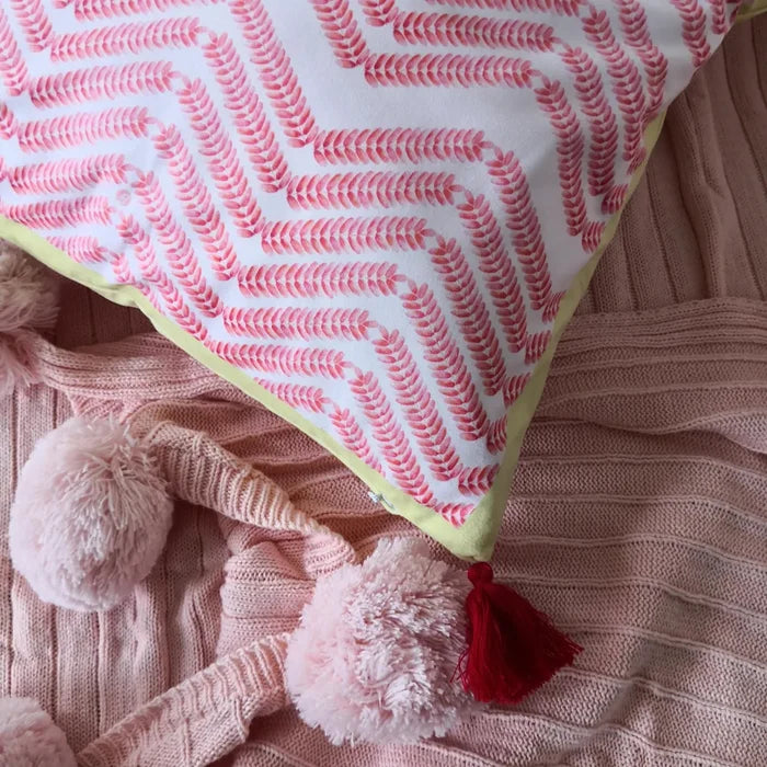 Close-up of pillow edge showing a red chevron pattern and red tassel on a pink ribbed blanket with pom-poms.