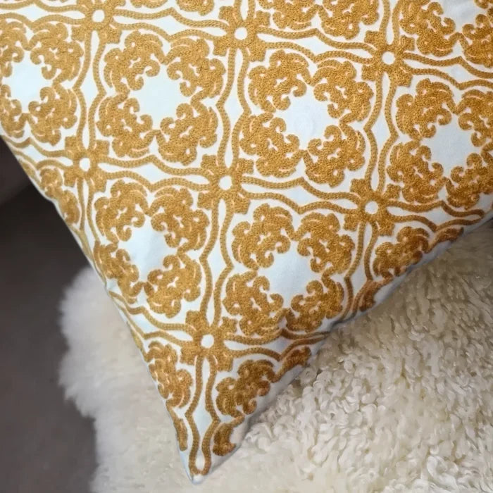 Close-up of a white pillow with golden embroidered pattern texture, on a fluffy white surface.