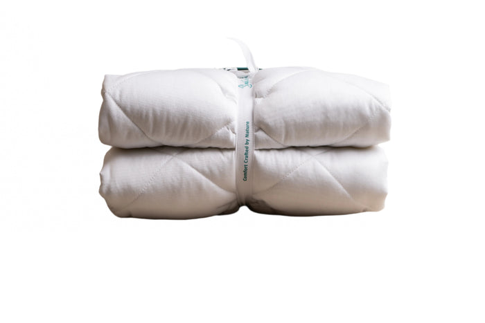 Two white quilted mattress protectors or blankets, neatly folded and bundled together with a band labeled 'Comfort Crafted by Nature